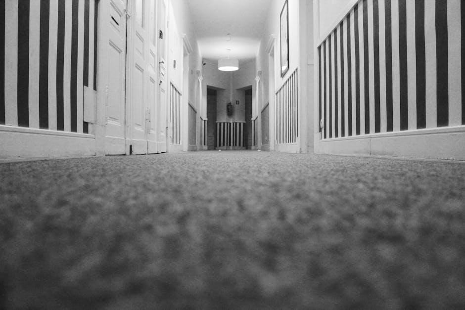 A person kneeling on a patterned carpet in a residential setting, using a yellow and black vacuum cleaner to perform surface cleaning. The individual is placing or retrieving a white cloth or filter i